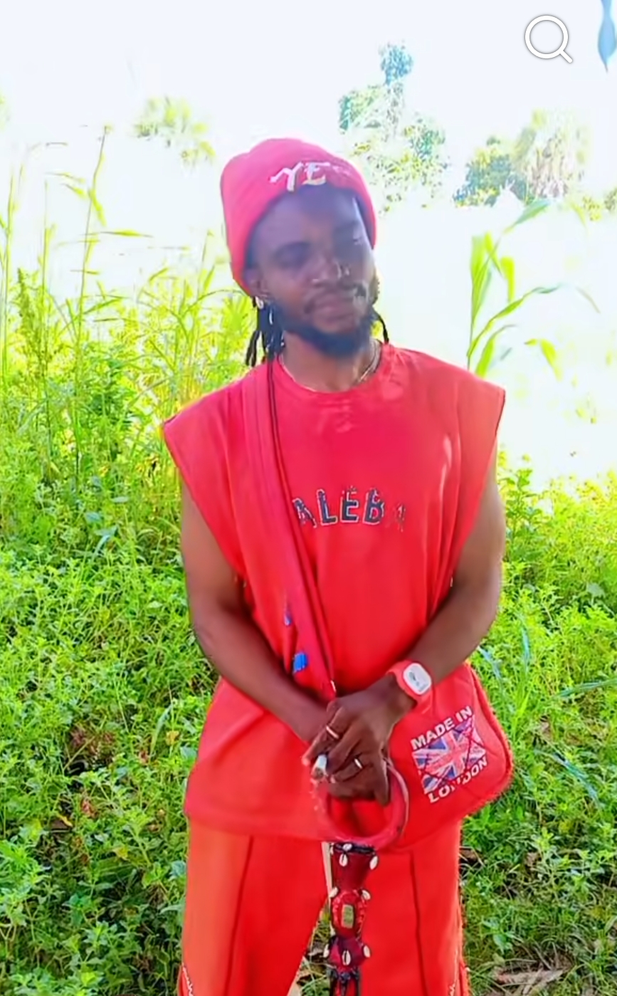 Man in a red cap, red sleeveless top and red trousers, standing among green plants in Benue State, identified as Zegebra.